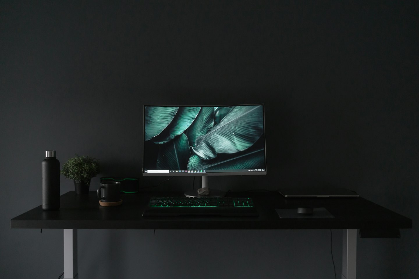 Modern desk with computer, plant, and mug in an office.