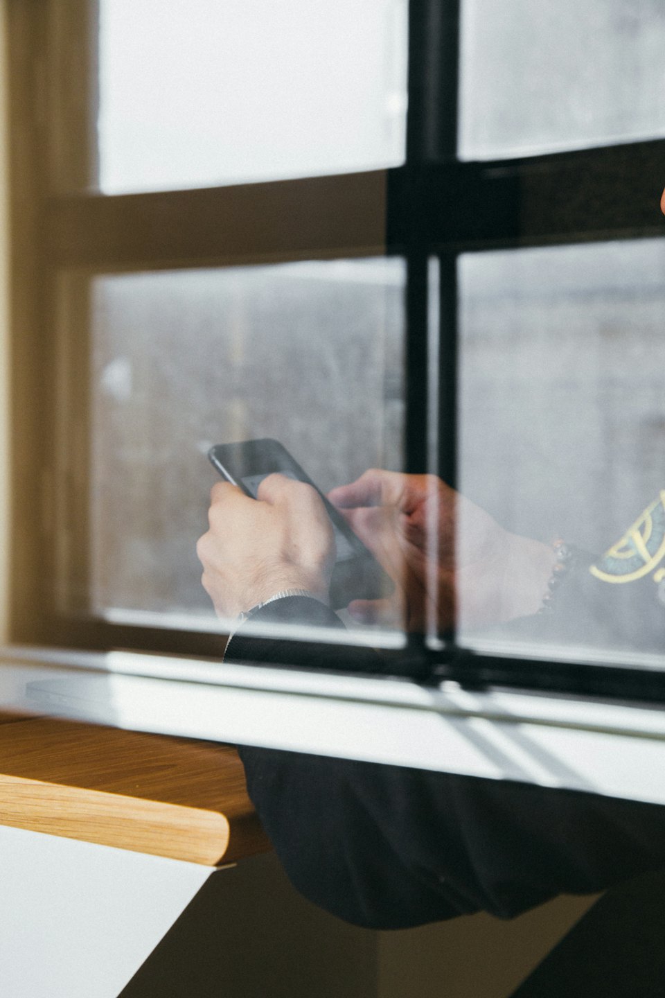 Hands holding a smartphone behind a reflective window.