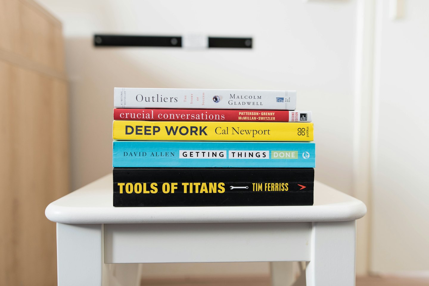 Five colorful self-help books stacked on a white stool.